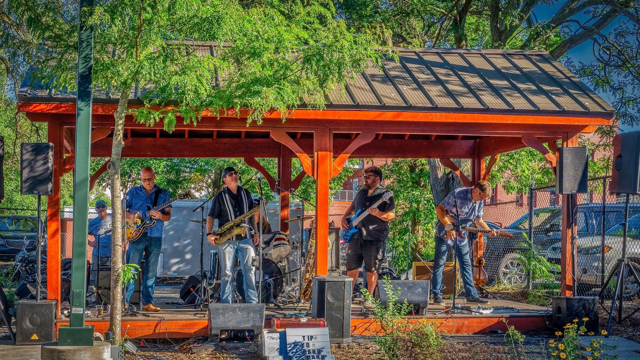 Photo of four men in a band playing outdoors under a small gazebo
