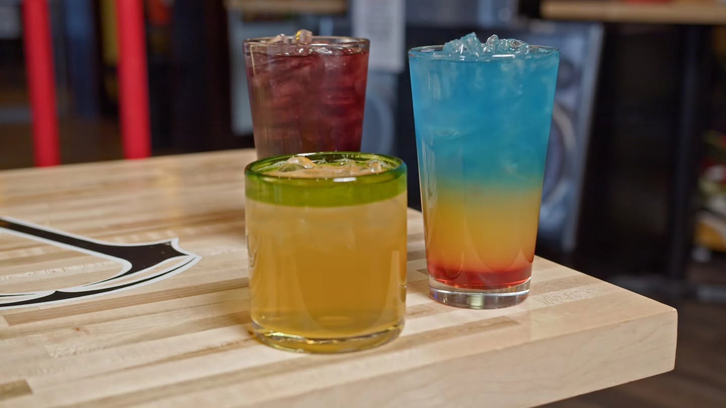 Three colorful cocktails lined up on a table
