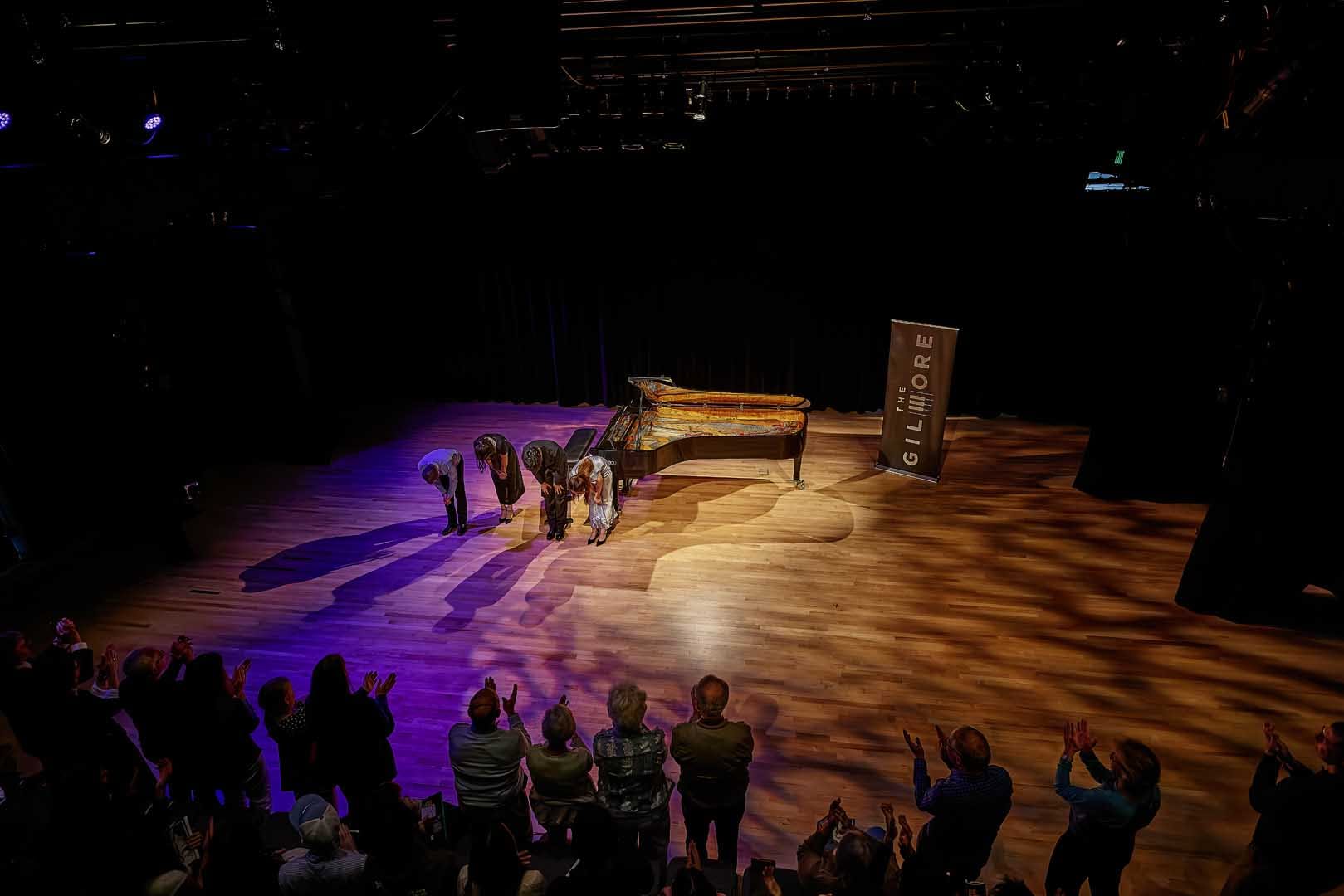 Three artists taking a bow on a dark stage with a piano behind them