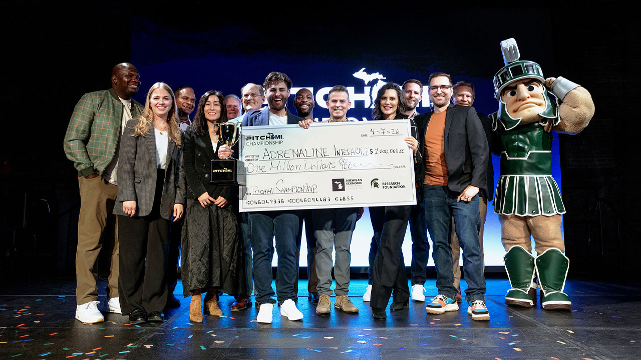 Photo of past PitchMI winners on a stage holding a large check